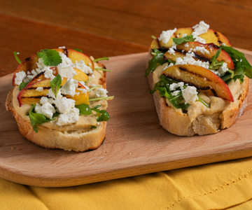 Tostada con hummus, melocotones a la parrilla, feta y rúcula