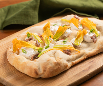 Pinsa con flores de calabacín, anchoas y crema de queso